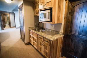 Kitchen with light stone counters, stainless steel microwave, light carpet, a sink, and baseboards