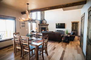 Dining room featuring baseboards, light wood-style flooring, beamed ceiling, an inviting chandelier, and a fireplace