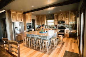 Kitchen featuring light stone counters, a center island, beam ceiling, light wood finished floors, and stainless steel appliances