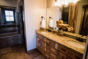 Full bath featuring double vanity, a garden tub, a notable chandelier, and a sink