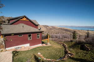 View of side of property with roof with shingles, a lawn, and a water view