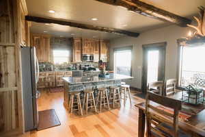 Kitchen featuring stainless steel appliances, beamed ceiling, light wood-type flooring, and a kitchen island