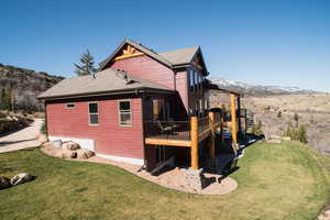 Back of property featuring stairs, a deck with mountain view, a lawn, and roof with shingles