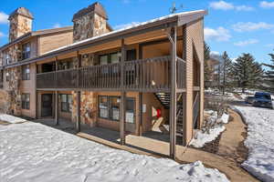 Snow covered back of property featuring stone siding, a chimney, and stairs