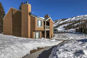 Snow covered house with stairs, a chimney, a mountain view, and stucco siding