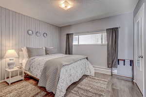 Bedroom with a textured ceiling, a baseboard radiator, and wood finished floors