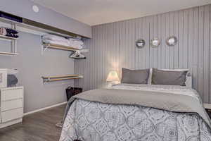 Bedroom with wood walls, a textured ceiling, baseboards, and dark wood-style flooring