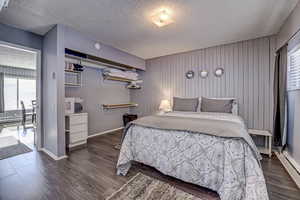 Bedroom featuring wood walls, baseboards, dark wood finished floors, and a textured ceiling