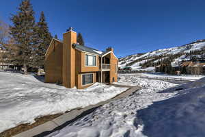 Snow covered property with a chimney, a mountain view, and stucco siding