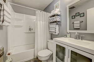 Full bath featuring toilet, shower / bathtub combination with curtain, visible vents, and vanity