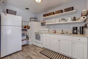 Kitchen featuring open shelves, light wood-style floors, white cabinetry, a sink, and white appliances