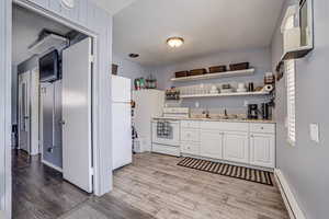 Kitchen with white appliances, white cabinetry, baseboard heating, open shelves, and light wood finished floors