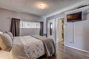 Bedroom with ensuite bath, a textured ceiling, baseboards, and wood finished floors