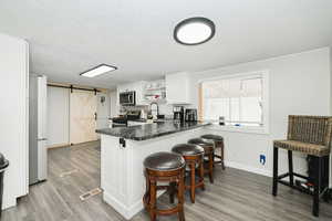 Kitchen with a barn door, a peninsula, stainless steel appliances, white cabinetry, and open shelves