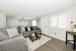 Living room featuring a chandelier, ornamental molding, wood finished floors, and baseboards