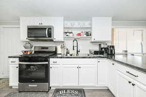 Kitchen featuring stainless steel appliances, a sink, white cabinetry, open shelves, and crown molding