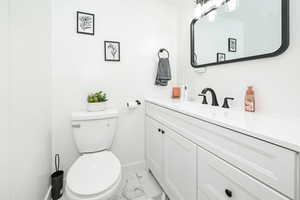 Bathroom featuring toilet, marble finish floor, baseboards, and vanity