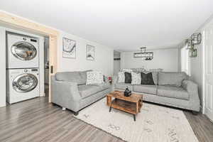 Living room with a chandelier, stacked washing maching and dryer, and wood finished floors