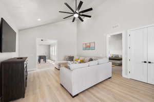 Living room featuring high vaulted ceiling, light wood-type flooring, visible vents, and ceiling fan