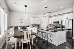 Kitchen with stainless steel appliances, dark countertops, white cabinetry, and a center island with sink