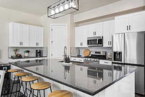 Kitchen with white cabinets, appliances with stainless steel finishes, a large island, and decorative light fixtures