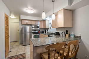 Kitchen featuring a breakfast bar, pendant lighting, stainless steel appliances, dark stone counters, and a peninsula