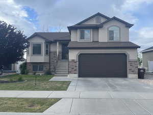 Split level home featuring a front lawn, brick siding, stucco siding, and a garage