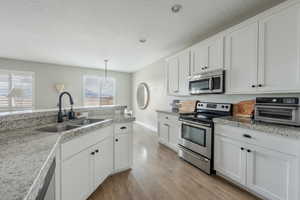 Kitchen with a toaster, stainless steel appliances, hanging light fixtures, white cabinetry, and a sink