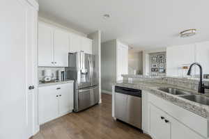 Kitchen with light stone counters, stainless steel appliances, white cabinets, a sink, and wood finished floors