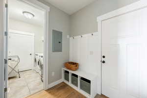 Mudroom with light wood finished floors, washing machine and dryer, electric panel, and baseboards