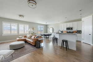 Living area with light wood finished floors, baseboards, a textured ceiling, and recessed lighting