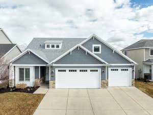 Craftsman-style home with driveway, a garage, a shingled roof, central AC unit, and stone siding