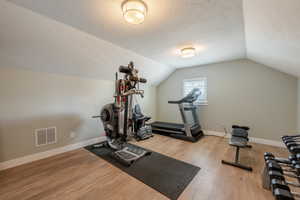 Exercise room featuring baseboards, visible vents, lofted ceiling, wood finished floors, and a textured ceiling