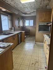 Kitchen with stainless steel appliances, wood walls, light countertops, brown cabinets, and light floors