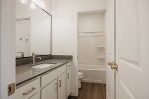 Bathroom featuring washtub / shower combination, vanity, toilet, and wood finished floors