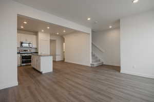 Kitchen featuring stainless steel appliances, white cabinets, open floor plan, light wood-type flooring, and a center island