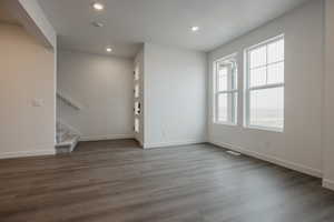 Unfurnished living room featuring baseboards, stairway, dark wood finished floors, and recessed lighting