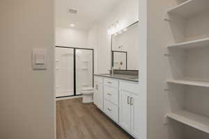 Bathroom with toilet, a sink, wood finished floors, double vanity, and a stall shower