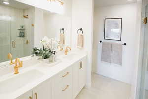 Full bathroom with a tile shower, double vanity, a sink, and baseboards