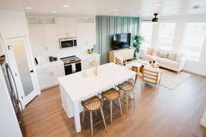 Kitchen with glass insert cabinets, stainless steel appliances, light countertops, white cabinetry, and a sink