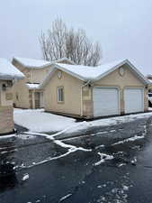 View of snowy exterior with driveway, brick siding, an attached garage, and stucco siding