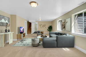 Carpeted living area featuring baseboards, stairs, and visible vents