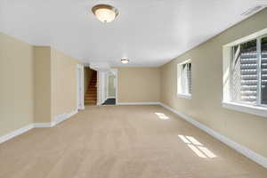 Carpeted empty room featuring visible vents, stairway, and baseboards