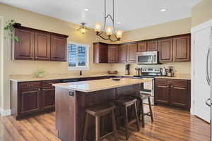 Kitchen with appliances with stainless steel finishes, a center island, pendant lighting, and light wood-style floors