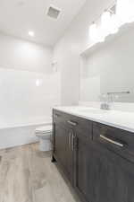 Bathroom featuring toilet, wood finished floors, vanity, bathing tub / shower combination, and visible vents