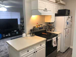 Kitchen with under cabinet range hood, electric range, white cabinetry, light countertops, and freestanding refrigerator