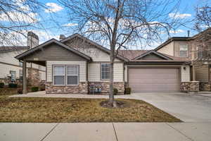 Craftsman-style home with a garage, stone siding, driveway, and a front lawn