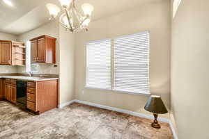 Kitchen featuring black dishwasher, light countertops, open shelves, brown cabinetry, and decorative light fixtures