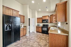 Kitchen with light stone counters, recessed lighting, a sink, black appliances, and brown cabinetry