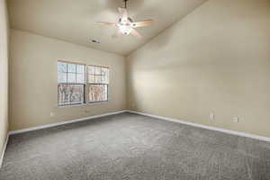 Carpeted spare room featuring a ceiling fan, visible vents, vaulted ceiling, and baseboards